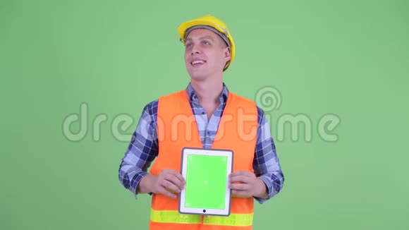 幸福的青年建筑工人一边思考一边展示数码平板电脑视频的预览图