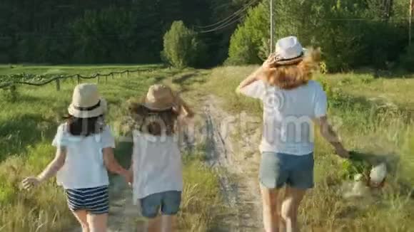 孩子们三个戴着帽子的女孩手牵着手沿着乡间小路跑回来视频的预览图