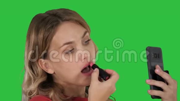 漂亮时尚的年轻女人在嘴唇上涂红色口红看着绿色屏幕上的手机屏幕Chroma键视频的预览图