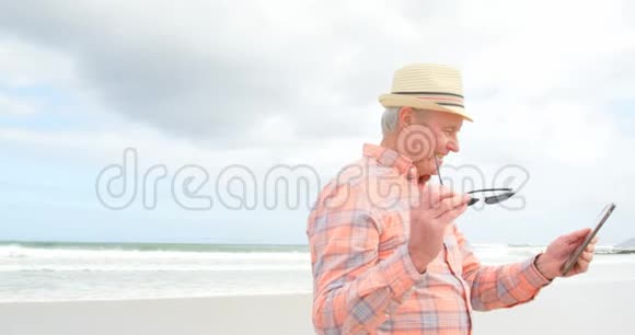 在海滩4k处使用数字平板电脑的老白种人老人的侧视图视频的预览图