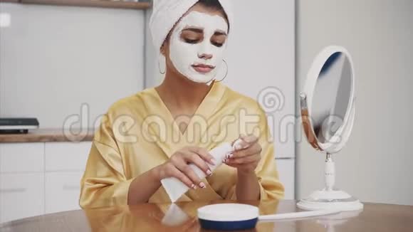 美容护肤和人理念微笑的年轻女人在脸上涂上面膜同时看镜子视频的预览图