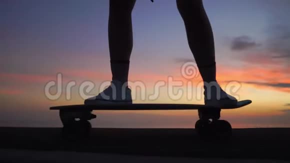 美丽的女孩骑着滑板在路上对抗夕阳的天空近点视频的预览图