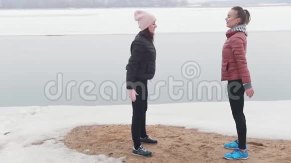 寒冷的天气两个穿夹克的苗条女人在雪地海滩上蹲着视频的预览图