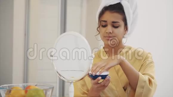 美容护肤和人理念微笑年轻女性应用面霜在家看镜子视频的预览图