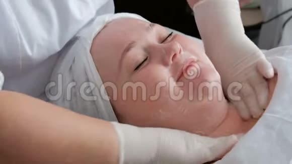 专业美容师的双手在一个丰满的女人的脖子和脸上涂上一种滋养或恢复活力的霜视频的预览图