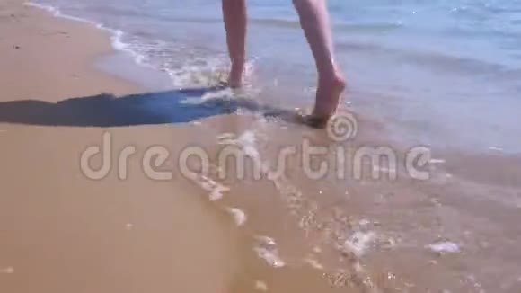 赤脚女游客在海边沙滩水中散步双腿特写视频的预览图