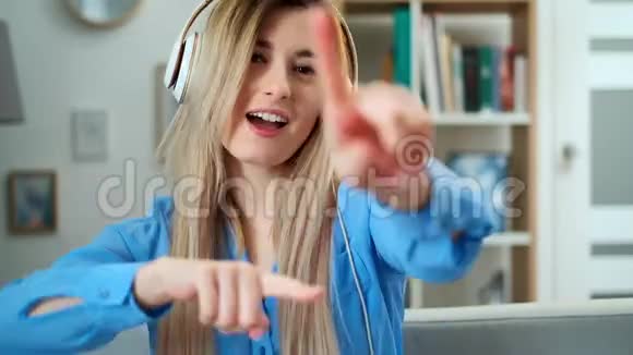 穿着蓝色服装在家欣赏音乐的年轻漂亮女孩的特写肖像女人听耳机音乐视频的预览图