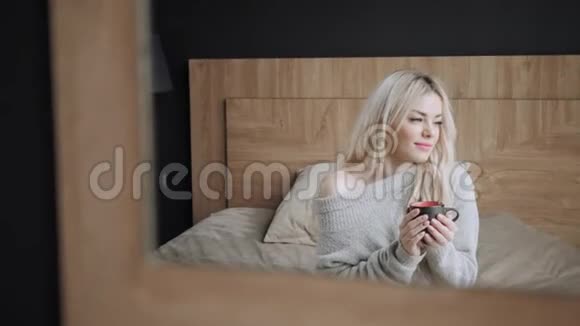 镜子里的倒影美丽的金发女人拿着陶瓷杯的茶或咖啡享受客房提供茶水时间视频的预览图