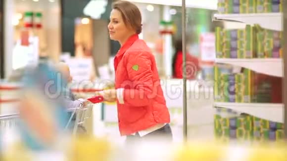 年轻的母亲和她的小男孩在超市穿着红色夹克的漂亮女孩在超市手推车里视频的预览图