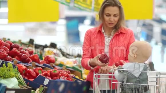 妈妈和宝宝在超市选择蔬菜一个女人向她一岁的儿子伸出一根红色的甜椒健康视频的预览图