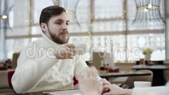 成年男子一边喝咖啡一边在咖啡馆里和女人说话视频的预览图