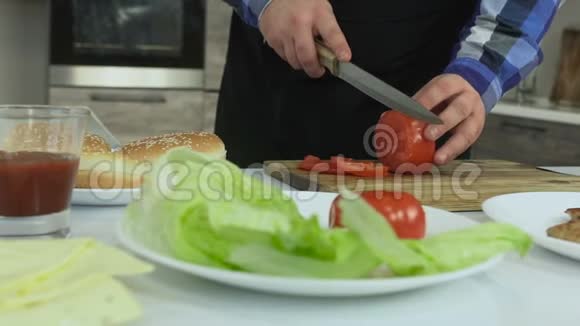 一个丰满的家伙在他的厨房里做汉堡包那个人在切割板上切西红柿不健康的生活方式油炸视频的预览图