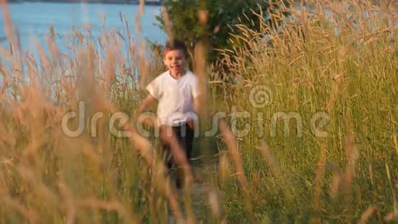 快乐的小男孩沿着小路跑过田野开心地笑着视频的预览图