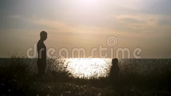 日落时分年轻人在海滩上牵着一个小男孩的手剪影父亲和他的儿子看着海景概念概念视频的预览图