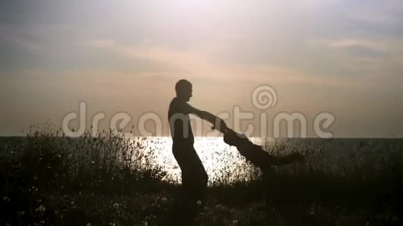 剪影快乐的父子在日落时在海滩上玩耍爸爸牵着孩子的手绕着他转视频的预览图