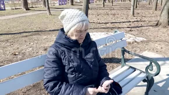 一位年长的妇女坐在公园户外的长凳上使用敲击智能手机她正在用智能手机视频的预览图