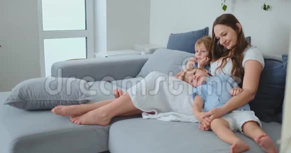 妈妈穿着裙子小孩子坐在沙发上看你最喜欢的电视剧视频的预览图