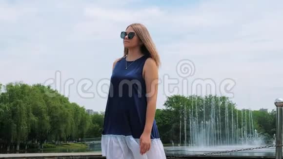 stadicam在喷泉附近的公园里拍摄了一个戴太阳镜的漂亮女孩可爱微笑的年轻女人视频的预览图