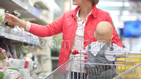 一个年轻的女人带着一个蹒跚学步的孩子在超市购物蔬菜和草药部套餐中的沙拉视频的预览图