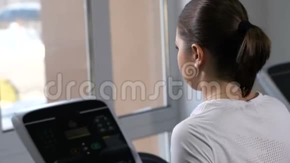一个女孩在体育俱乐部的跑步机上跑步黑发扎成马尾4K慢慢视频的预览图