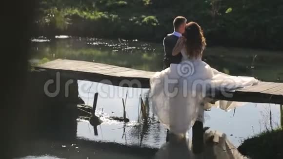 新娘坐在河边的一座木桥上一对幸福的家庭夫妇花时间在公园里视频的预览图