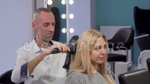 成熟的男理发师在美容院吹干女客户的头发视频的预览图