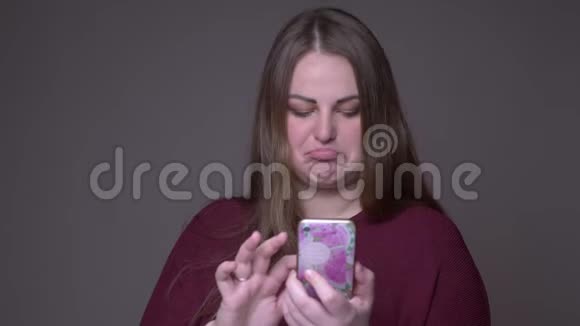 年轻超重的白种人女性手机短信特写背景与灰色隔离视频的预览图