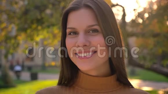 在绿色公园背景下年轻的黑发女孩带着真诚的微笑观看镜头的特写肖像视频的预览图