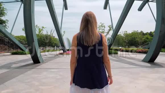 斯塔迪加姆的后景拍摄了一个穿着蓝色裙子的漂亮女孩在公园里走到喷泉前视频的预览图