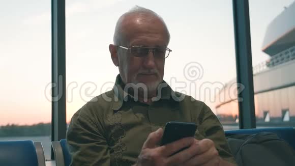一位白发苍苍胡须苍白的老人正在机场等候登机他用智能手机打发时间视频的预览图