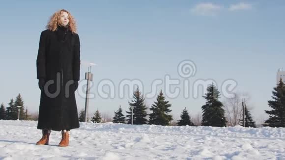 穿着黑色冬衣的年轻女子站在蓝天跟踪镜头前视频的预览图