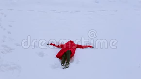 年轻女子躺在雪地上双手在雪地上移动画着天使的假翅膀视频的预览图