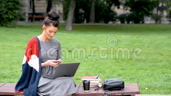 微笑的女学生在公园里坐坐在公园的笔记本电脑视频的预览图
