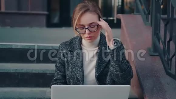 戴眼镜和外套的漂亮女孩在户外使用笔记本电脑视频的预览图