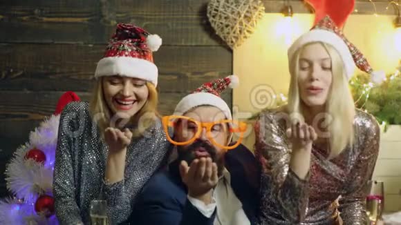 戴着大眼镜的长胡子男人和两个戴着帽子的少女在新年的背景下用手掌吹糖果视频的预览图