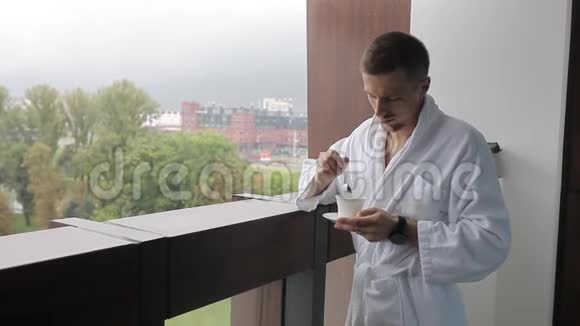 一个年轻人一个穿着白色外套的男人在阳台上喝咖啡视频的预览图