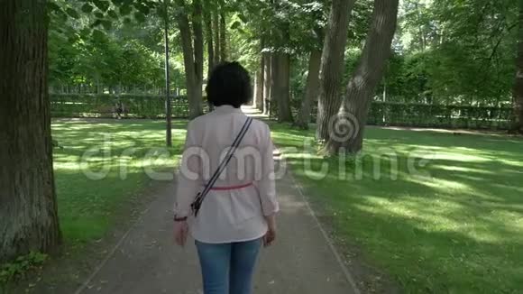 夏天一个女人在阴凉的公园里沿着小径散步视频的预览图