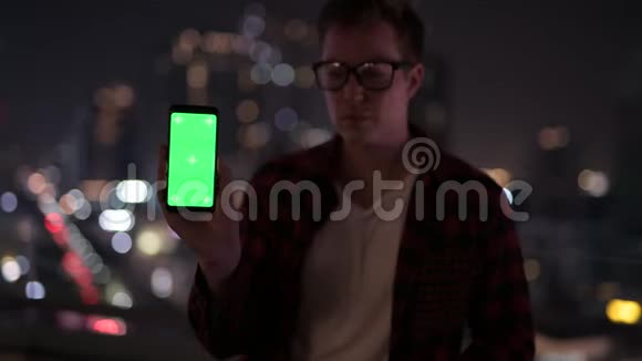 年轻快乐的嬉皮士晚上对着城市的景色展示电话视频的预览图