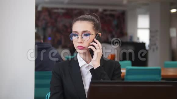 商业概念一个戴眼镜的女人坐在桌子旁用电话说话视频的预览图