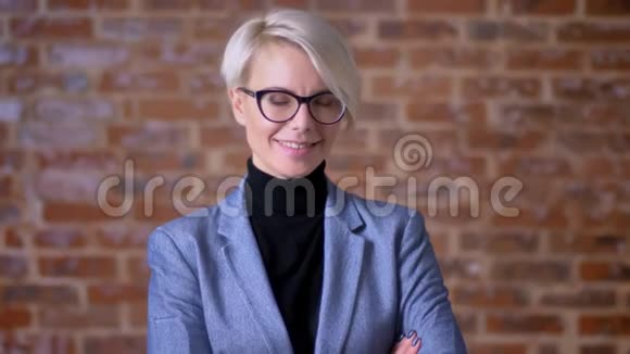 戴眼镜的中年金发短发女人的肖像对着镜头微笑在布里克肯的墙背景上点头视频的预览图