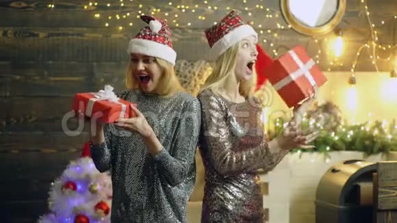 女孩对新年礼物感到高兴令人惊讶的是穿着银色连衣裙和戴着红色帽子的快乐金发女郎在庆祝新年视频的预览图
