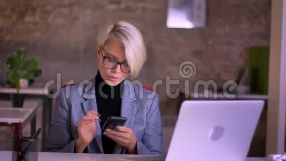 中年短发女商人戴着眼镜看着智能手机在办公室里笑着的肖像视频的预览图