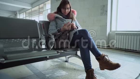 坐在火车站的年轻女人带着智能手机的肖像视频的预览图