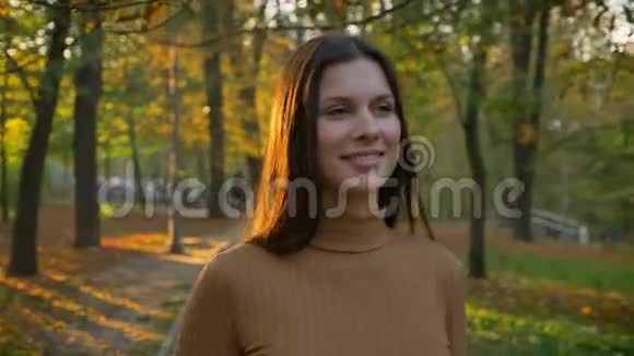 美丽年轻的白种人女孩在秋天公园散步的肖像头发里透着阳光视频的预览图