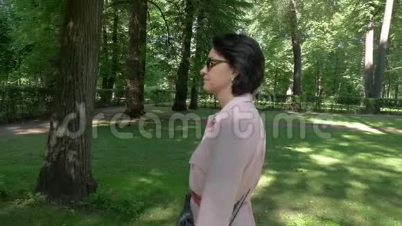 夏天一个女人在阴凉的公园里沿着小径散步视频的预览图