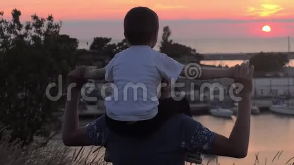 大海上美丽的日落小男孩坐在爸爸的肩膀上看上去游艇和帆船停泊在码头上视频的预览图