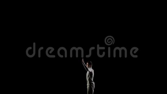 穿着白色衣服黑色背景的英俊男体操跳在蹦床侧面视频的预览图