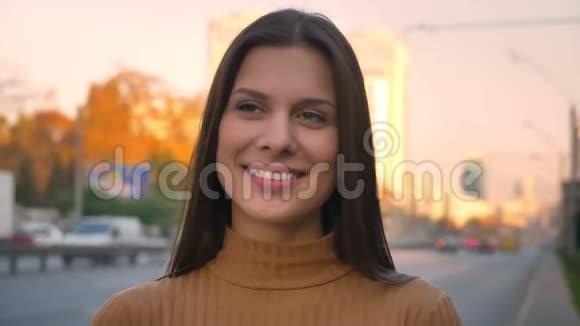 一幅漂亮的黑发女孩的特写肖像转向镜头在道路背景上真诚的微笑视频的预览图