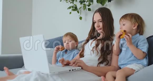 漂亮的年轻妈妈和两个小男孩正在看手提电脑屏幕的家庭照片做网上购物视频的预览图