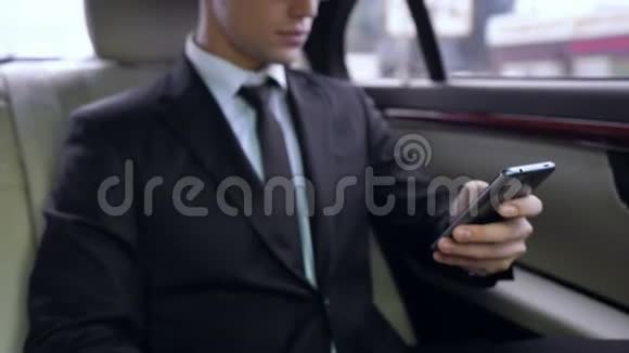 穿西装的年轻男性在乘坐商务车时在智能手机上发短信视频的预览图